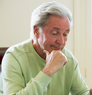 older adult man sitting with hand to his chin looking down contemplating