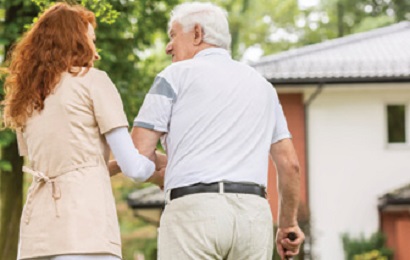 adult woman helping older adult man walk with cane outside