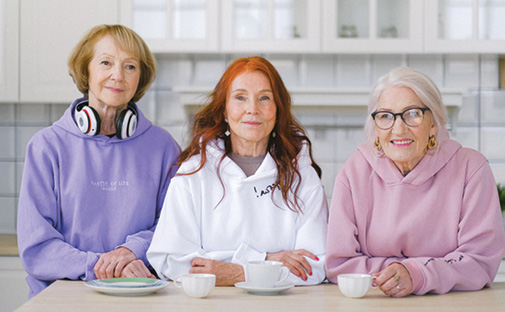 three older adult women sitting at table facing for photo